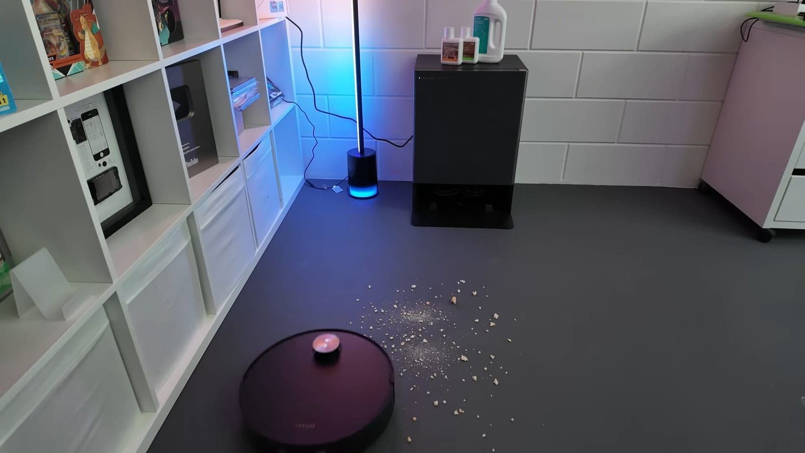 Dreame Matrix 10 Ultra robot leaving its tall docking station toward crumbs on a gray studio floor
