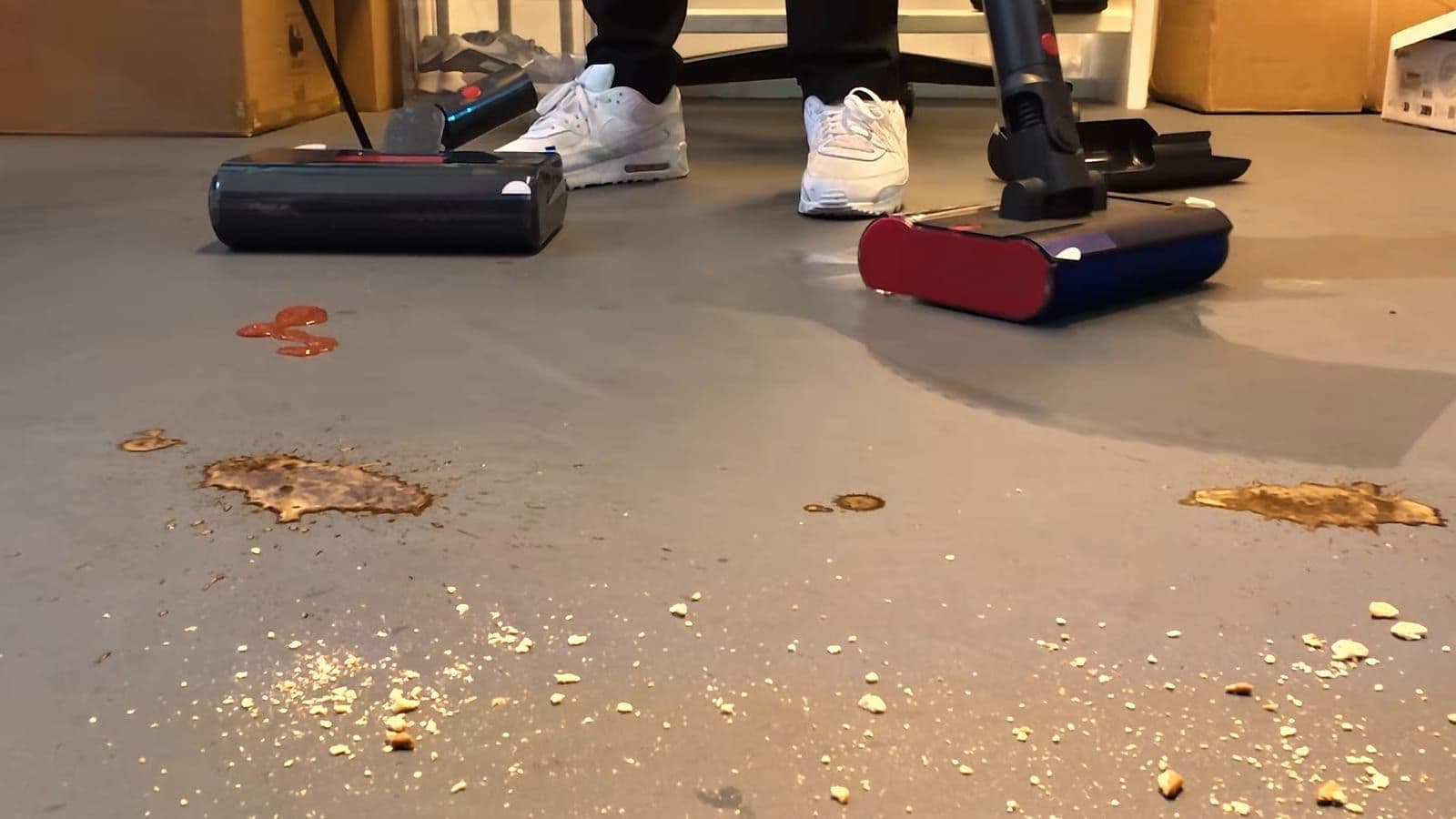 Twee Dyson wasmonden op een grijze vloer naast ketchup, koffievlekken en kruimels, met een natte strook achter een van de koppen