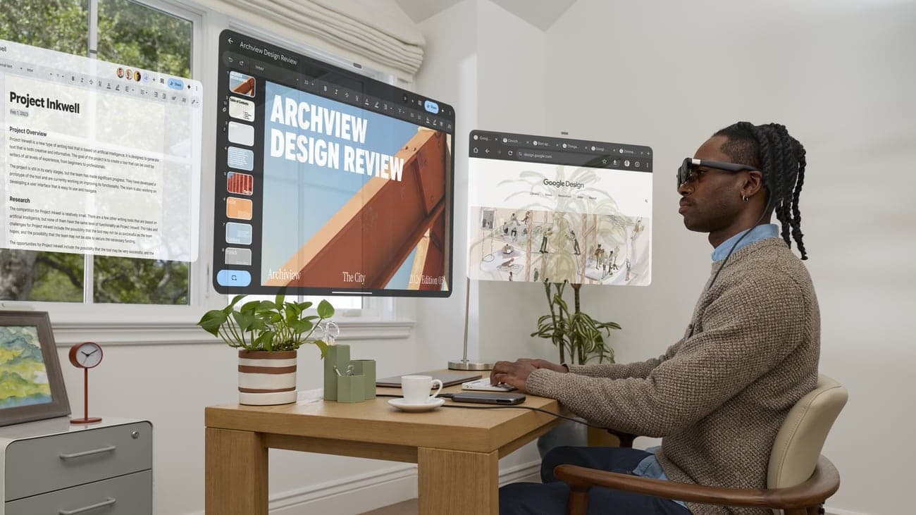 Man aan een houten bureau met de XREAL Aura-bril op terwijl er drie virtuele werkvensters in de lucht zweven
