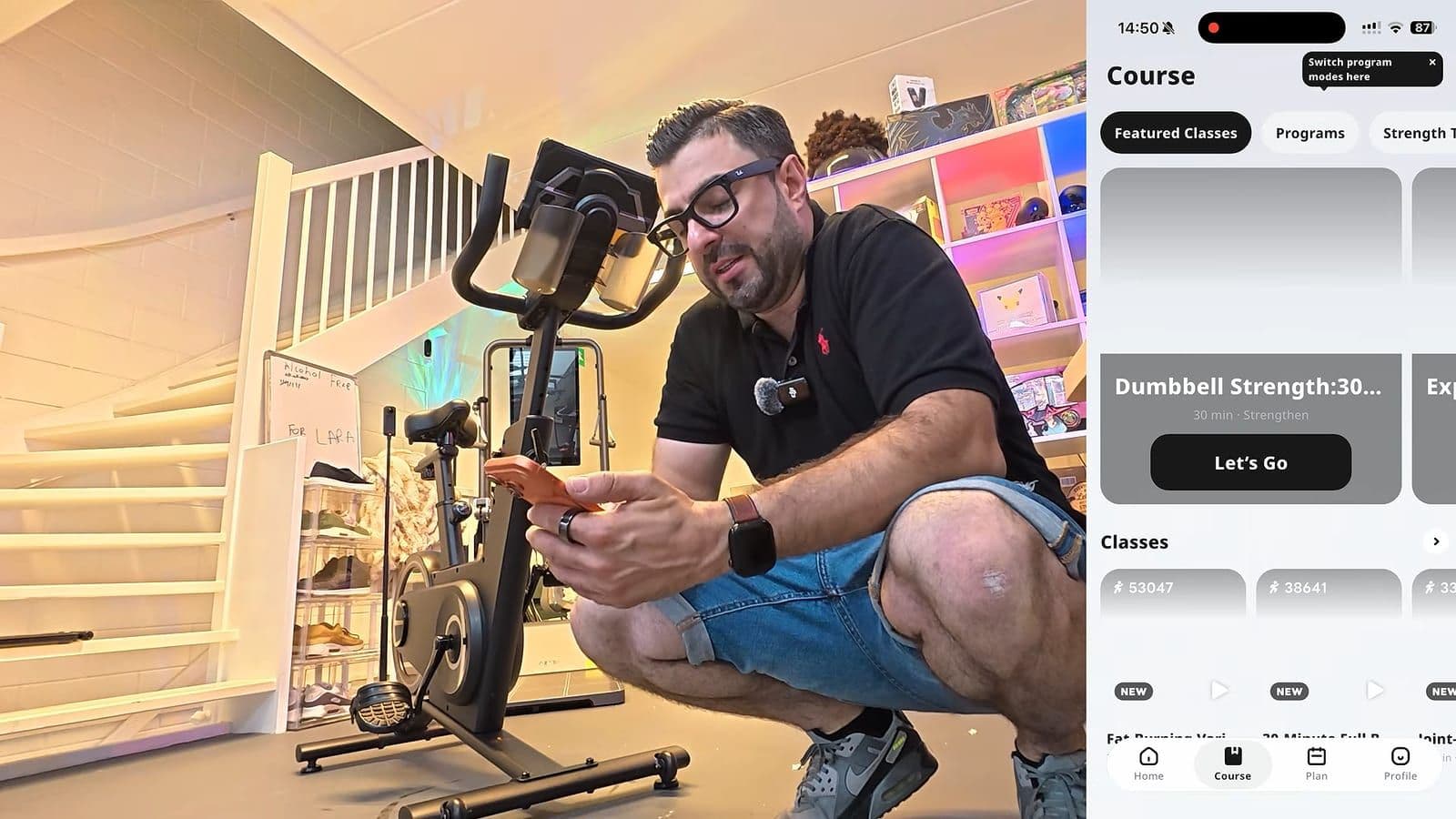 Zino hurkt naast de spinningfiets met zijn telefoon, rechts de KS Fit app met lessen en programma's